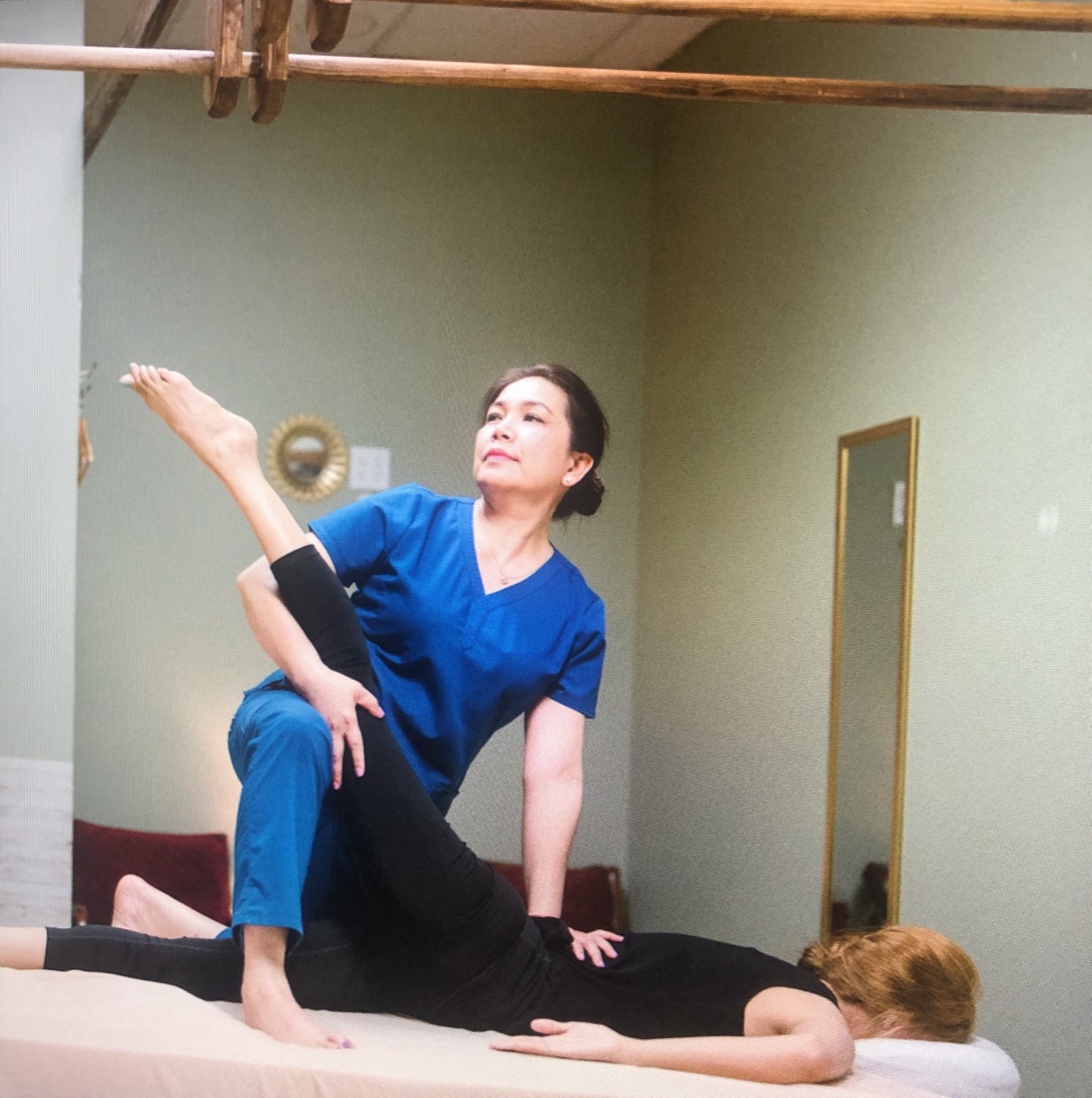 Nina, founder of Magnolia Wellness Massage, guiding a client through a traditional Thai stretch